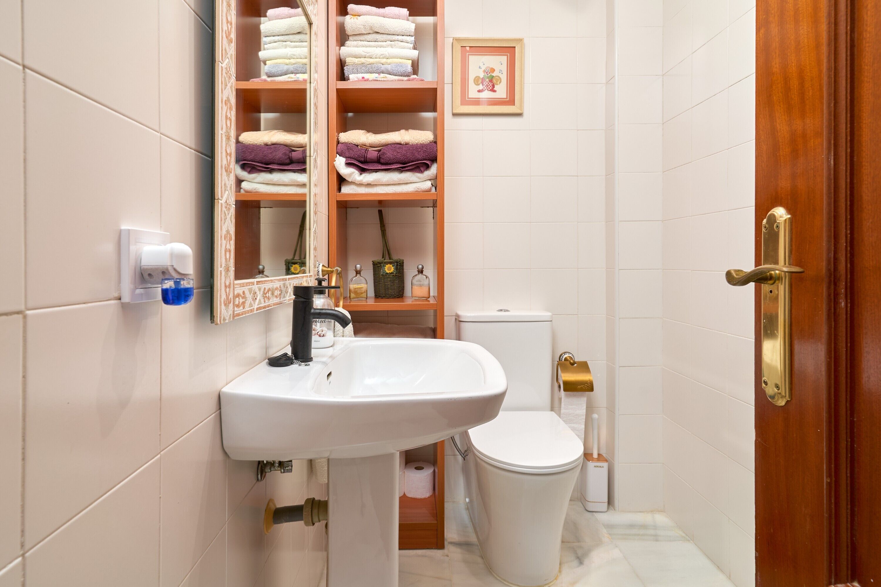 Een badkamer met een wit wastafelmeubel, toilet, spiegel en een plank met handdoeken.