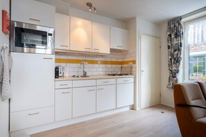 A modern kitchen with white cabinets, a microwave, a stove, and a sink. - Holiday home with garden in Aagtekerke | Dorpsplein 25 (Aagtekerke)