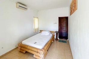 A room with a single bed, a wooden door, a small table, and an air conditioning unit.