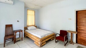 A room with a bed, a chair, a small table, a red chair, a wooden door, and an air conditioning unit. - Cozzy HEPI Bungalo Lovina Singaraja Bali (Buleleng)