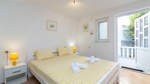 Une chambre à coucher comprenant un lit, deux tables de chevet avec des lampes, une fenêtre avec des stores et une porte donnant sur un espace extérieur.