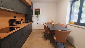 Une cuisine moderne avec des meubles de couleur sombre, un plan de travail en bois et un coin repas comprenant une table et des chaises.