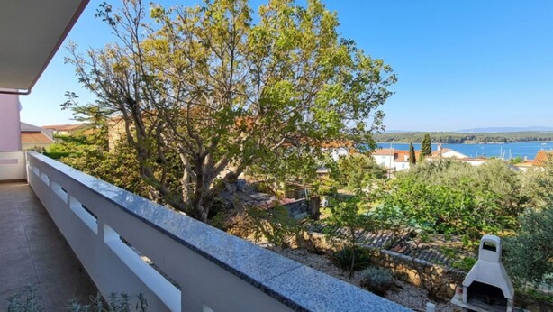 Een balkon met uitzicht op een boom, een stenen muur en een waterpartij.