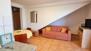Een kleine kamer met een bed, een tafel, een bank, een spiegel en een televisie.