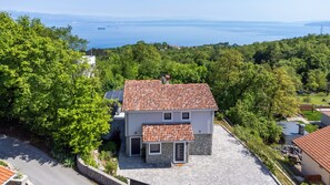 Ein zweistöckiges Haus mit Ziegeldach, umgeben von üppiger Vegetation und Blick auf das Meer.