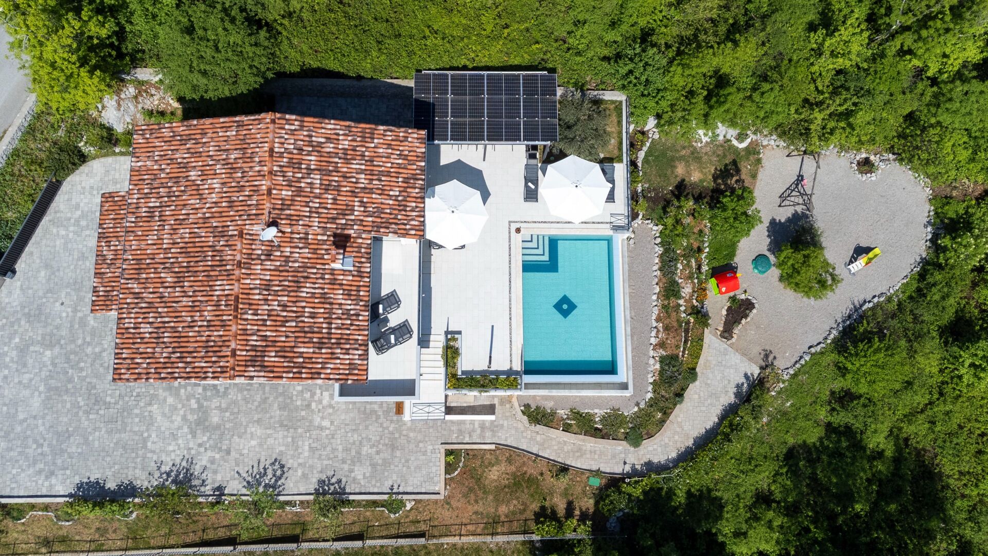 A rooftop with a swimming pool, solar panels, and a fenced garden area.