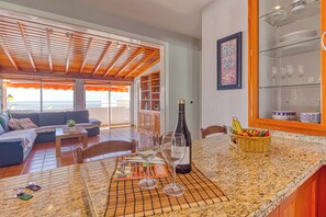 A kitchen with a granite countertop, a dining area with a table set for two, and a view of the beach through the open door.