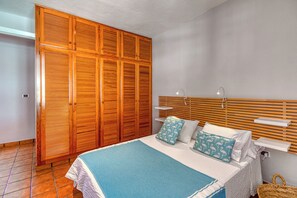 A bedroom with a bed, wooden wardrobe, bedside tables, and a wall-mounted shelf.