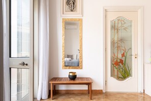 Ein Zimmer mit einem großen Spiegel, einer Holzbank mit einer Schüssel, einer Tür mit einer floralen Glasverkleidung und einem Fenster mit Vorhang.
