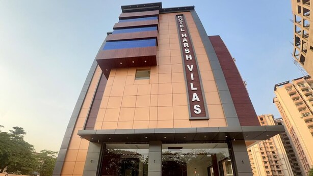 A modern hotel with a prominent vertical sign, a central entrance, and a surrounding paved area. - Hotel Harsh Vilas (Basai)