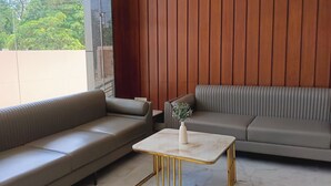 A modern living room with two sofas, a small table, and a view of greenery outside. - Hotel Harsh Vilas (Basai)