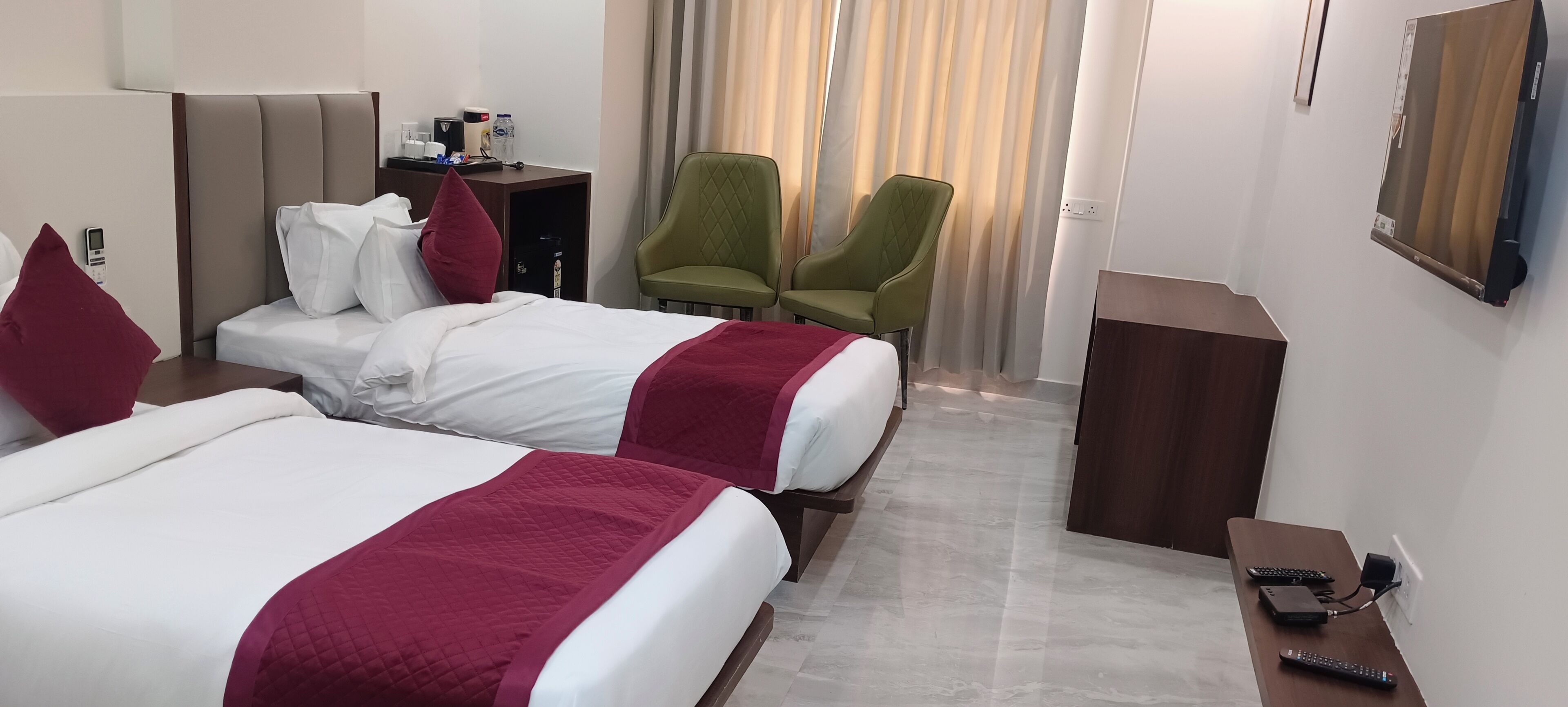 Ein Hotelzimmer mit zwei Betten, einem Schreibtisch, einem Stuhl, einem Fernseher und einer Fernbedienung.