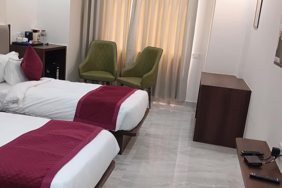 A hotel room with two beds, a desk, a chair, a TV, and a remote control.