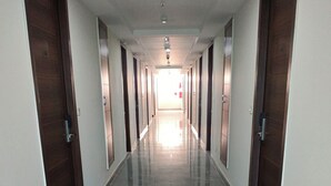 A long, narrow hallway with doors on both sides, leading to a bright room at the end. - Hotel Harsh Vilas (Basai)
