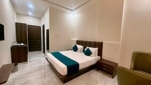 A modern hotel room with a large bed, a bedside table, a chair, and a desk with a chair. - Hotel Harsh Vilas (Basai)
