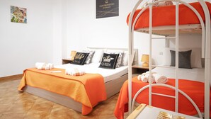 Habitación de hotel con dos camas, una de ellas litera, ropa de cama anaranjada y almohadas decorativas.