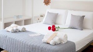 Una cama bien hecha con toallas enrolladas y un ramo de rosas rojas, un mesita de noche blanca y un adorno de pared.