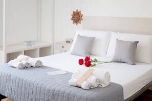A neatly made bed with rolled towels and a bouquet of red roses, a white nightstand, and a decorative wall piece. - Double Room with Private Balcony and Sea View (Porto Cesareo)