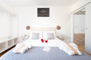 Una camera d'albergo con un letto, due comodini, un tavolino e un cartello a parete, oltre a una porta con vista.