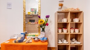 Un área de recepción con una mesa que exhibe bocadillos y un jarrón con flores, un espejo con marco dorado y una estantería con tazas y una máquina de café.