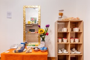 A reception area with a table displaying snacks and a vase of flowers, a mirror with a gold frame, and a shelf with cups and a coffee machine. - Double Room with Private Balcony and Sea View (Porto Cesareo)
