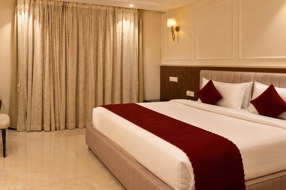 Ein Hotelzimmer mit einem großen Bett, einem Kopfteil mit einer Leuchte und einem Vorhang.