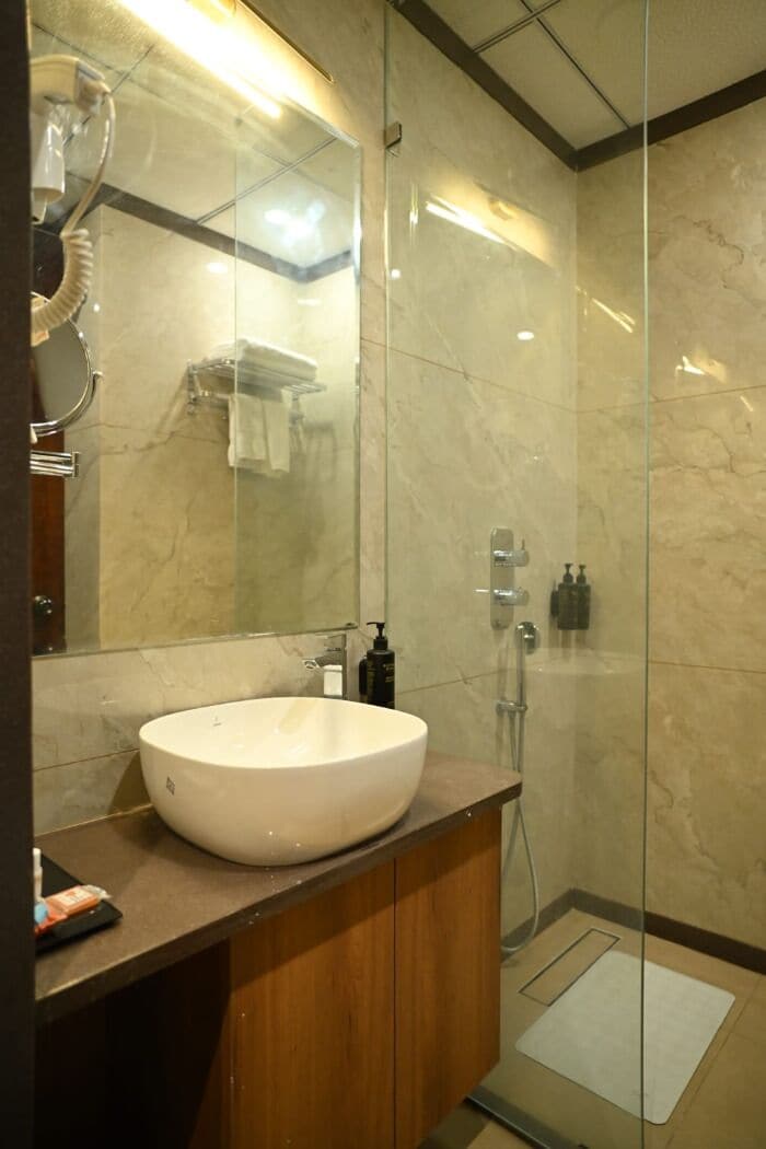 A modern bathroom with a large oval sink, a glass shower enclosure, and a marble-tiled wall.