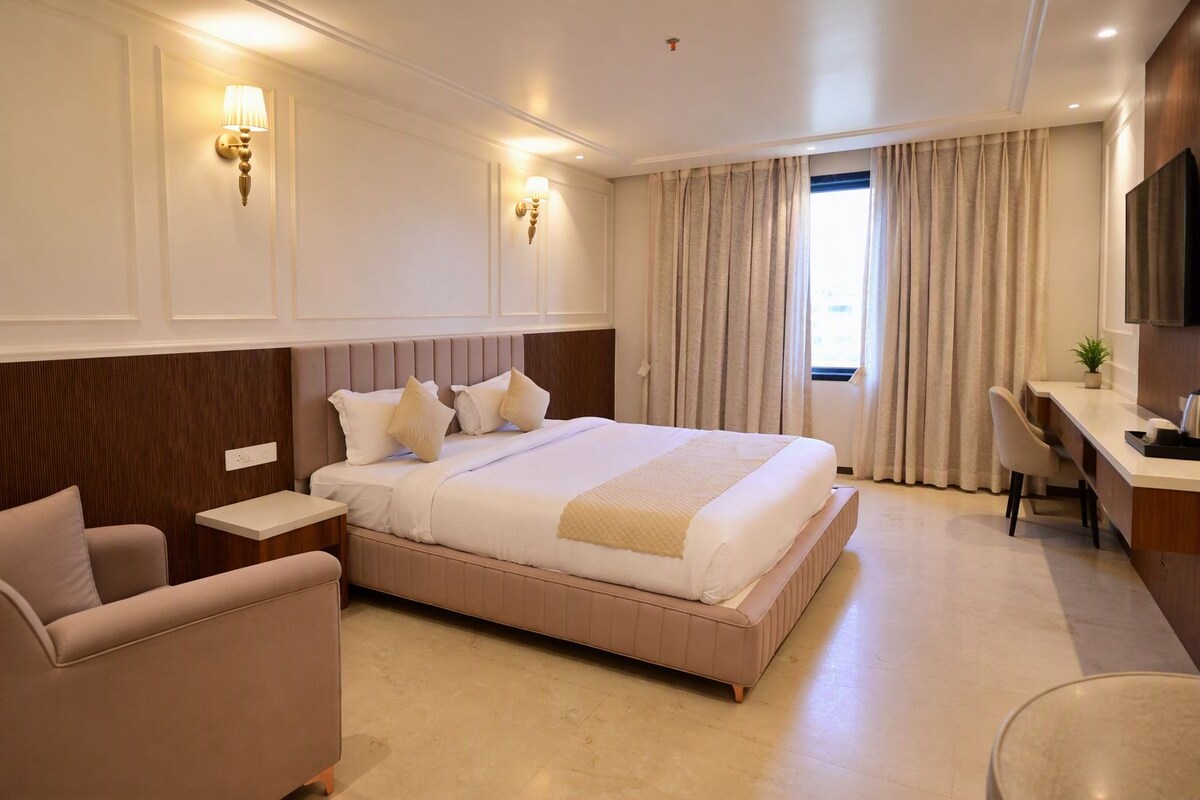 Ein Hotelzimmer mit einem großen Bett, einem Schreibtisch, einem Sessel und einem Fernseher.