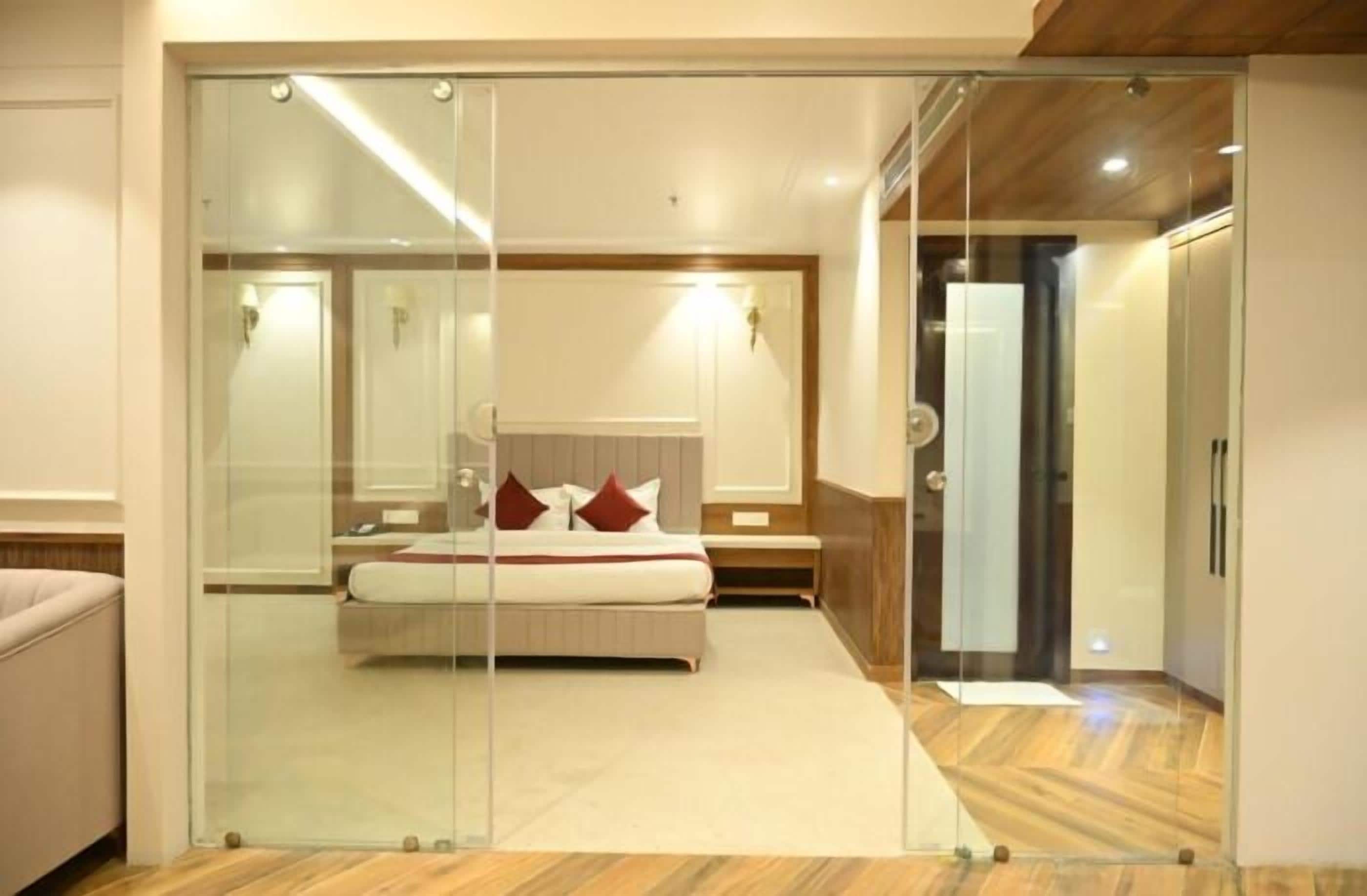 A bedroom with a glass partition, a bed with red pillows, and a wooden floor.