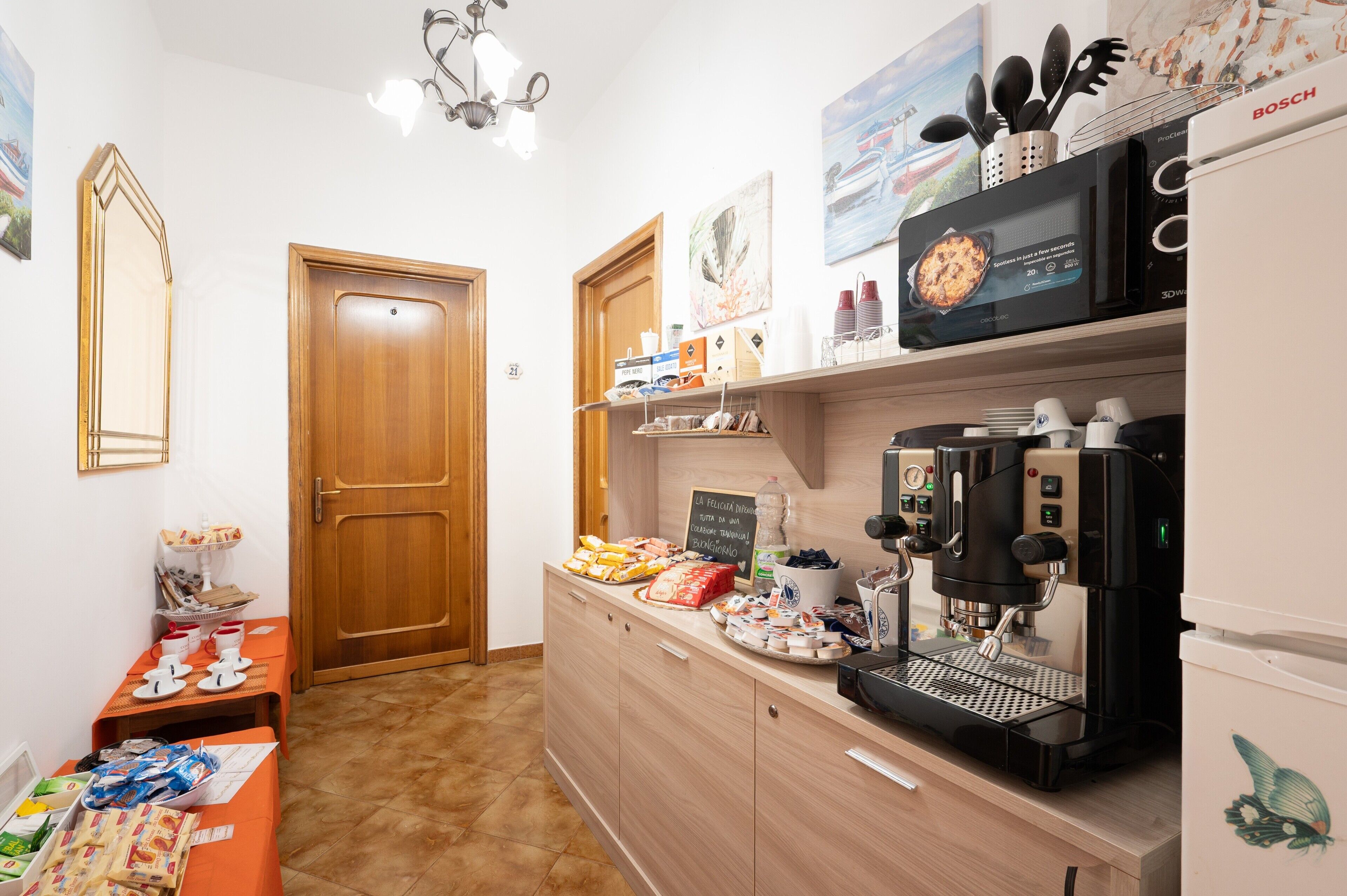 Ett litet kök med en kaffemaskin, mikrovågsugn och diverse matvaror på bänken.