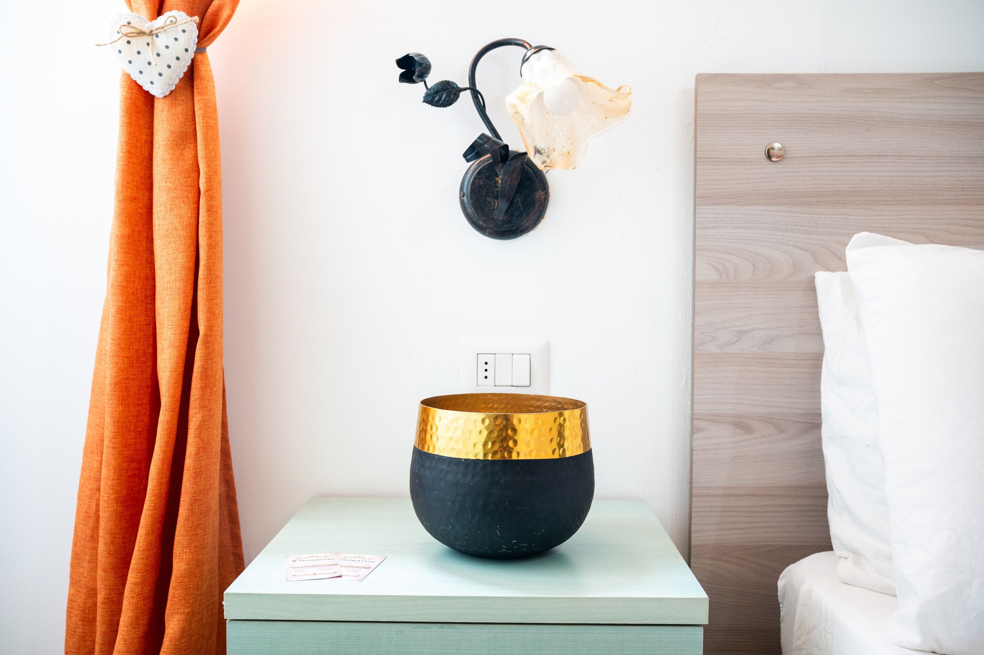 Una habitación con una mesita de noche, una lámpara de pared, una cortina y una cama.