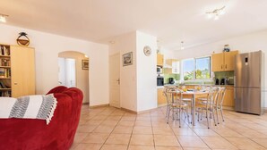 Een modern appartement met een rode bank, een eethoek met stoelen, een keuken met apparatuur en uitzicht door het raam.