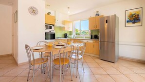 Een moderne keuken met een eettafel, stoelen, een koelkast en een klok aan de muur.