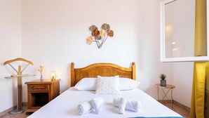 Een net opgemaakt bed met handdoeken, een houten nachtkastje met een lamp en een decoratie aan de muur.