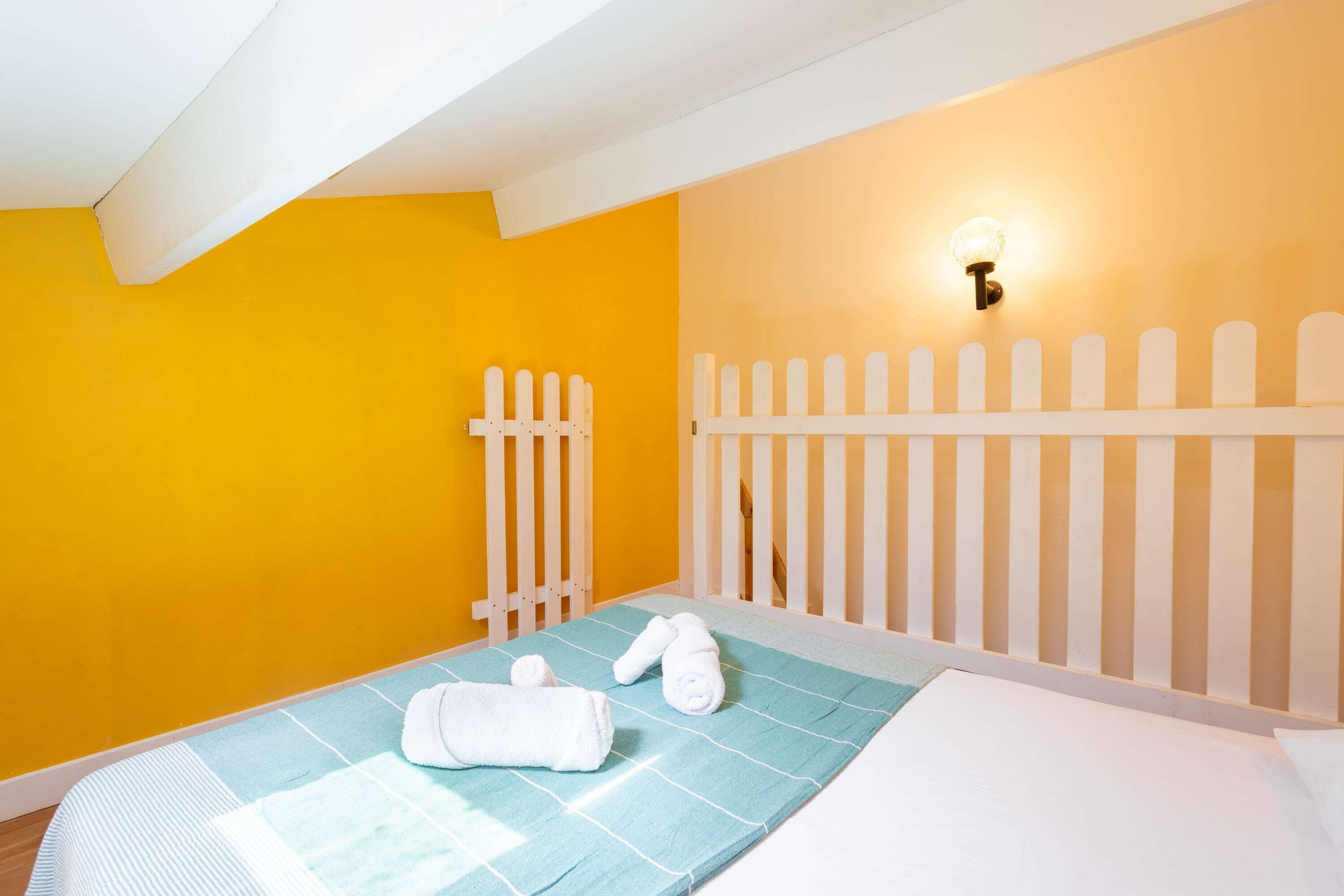 Une pièce avec un lit, une clôture blanche en bois et un luminaire fixé au mur.