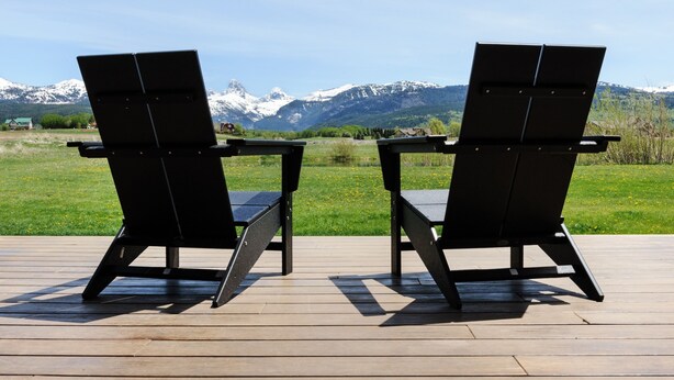 Två svarta Adirondack-stolar står på ett trädäck med utsikt över snöklädda berg.