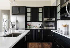 A modern kitchen with dark cabinetry, a stainless steel refrigerator, an oven, and a sink. - Modern Teton View Home in Driggs w/AC (Driggs)