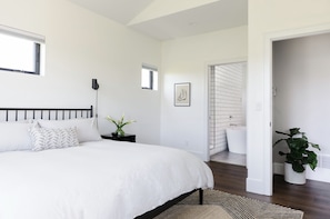 A bedroom with a bed, bedside table, potted plant, and a view of the bathroom. - Modern Teton View Home in Driggs w/AC (Driggs)