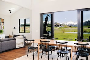 A modern living room with a large dining table, black chairs, a grey sofa, and a bookshelf. - Modern Teton View Home in Driggs w/AC (Driggs)