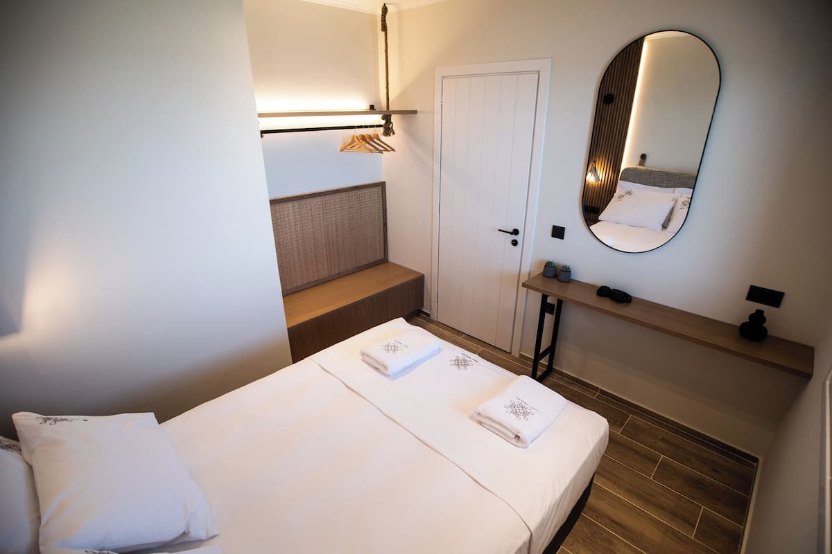 Een hotelkamer met een bed, nachtkastje, spiegel, hanglamp en een deur.