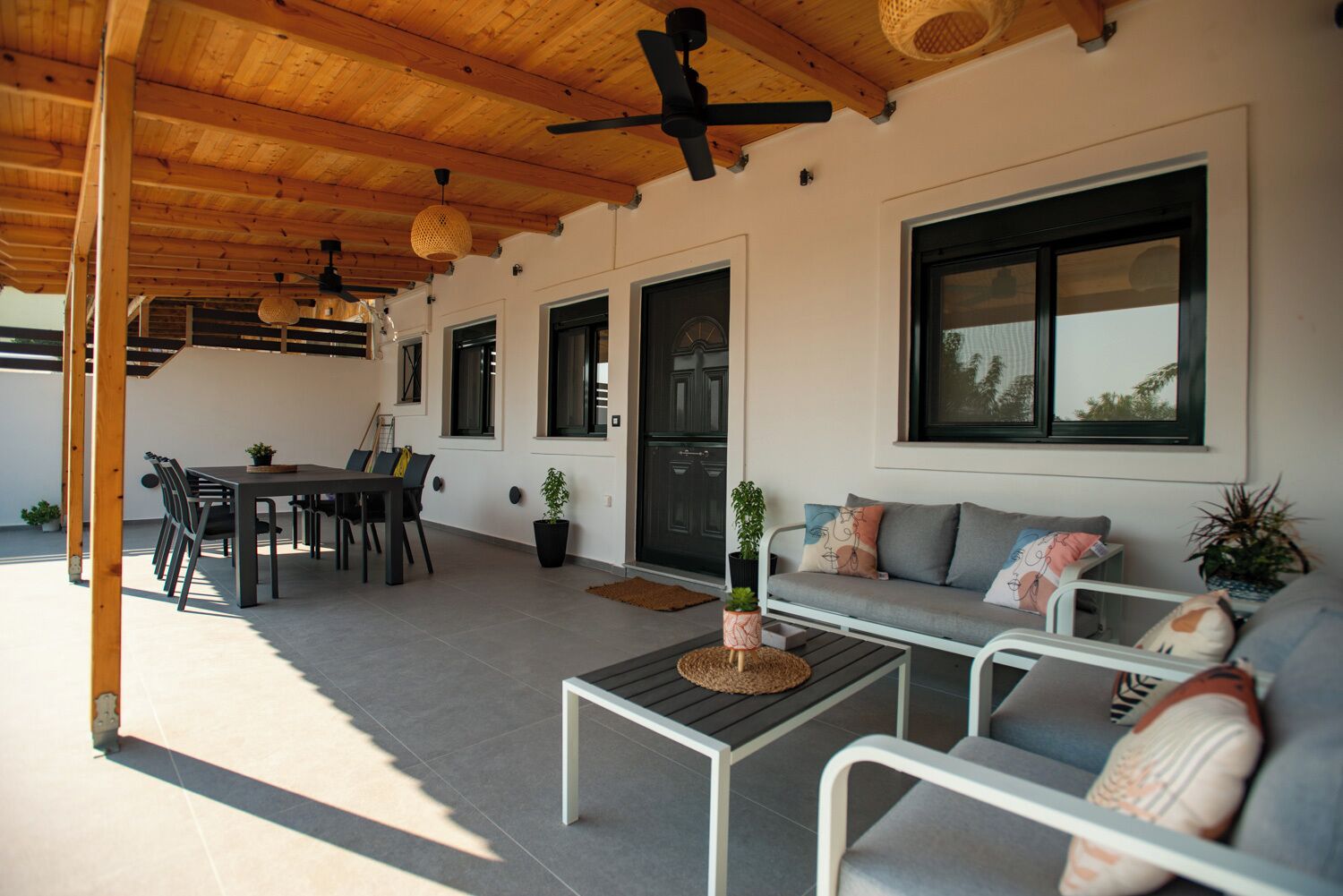 En overdækket terrasse med spisebord, stole, sofa og sofabord.