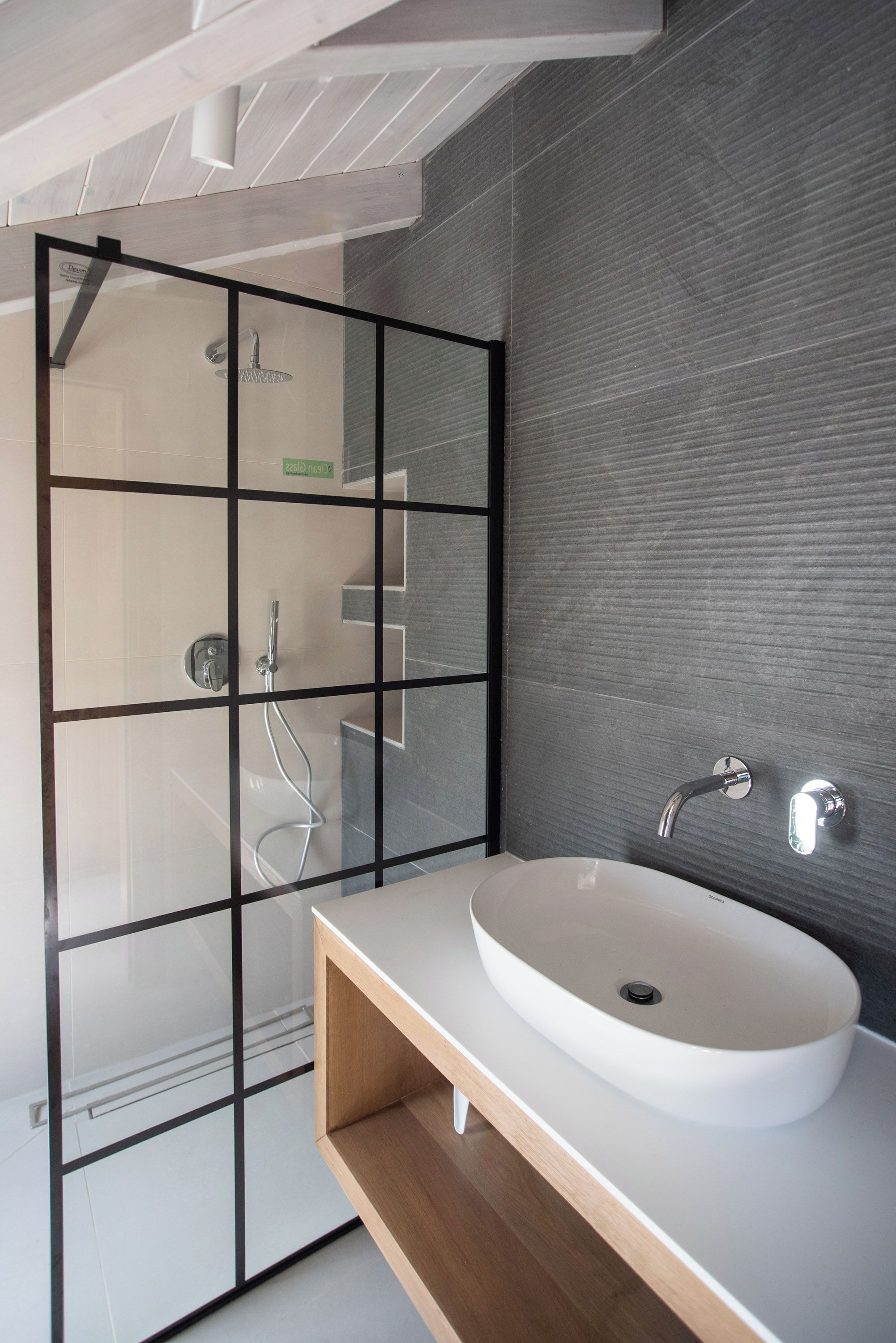 A modern bathroom with a glass shower enclosure, a white sink, and a wooden vanity.