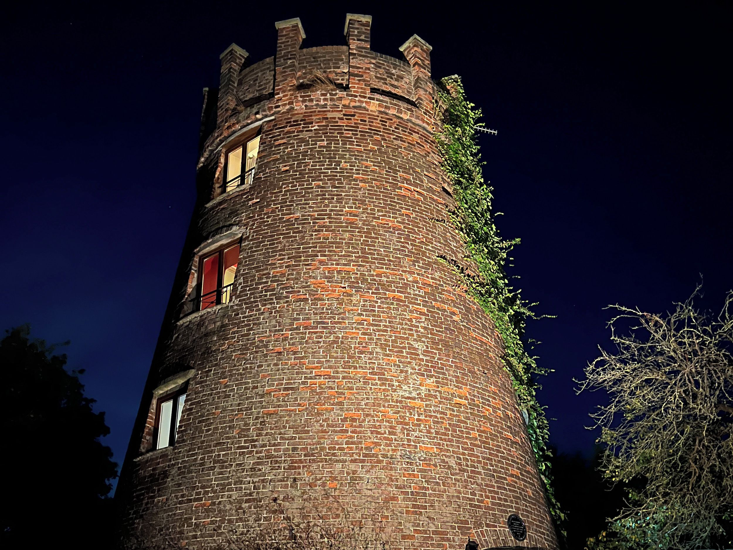 A tall, cylindrical brick tower with windows and a chimney, surrounded by trees.