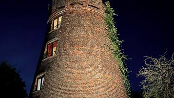 A tall, cylindrical brick tower with windows and a chimney, surrounded by trees.