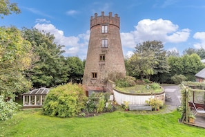 A brick tower with windows, surrounded by a garden with various plants and a conservatory. - Hadley Park Windmill (Telford)
