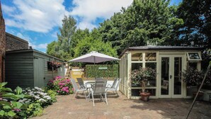 A patio area with a table and chairs, a hanging flower basket, and a small shed. - Hadley Park Windmill (Telford)