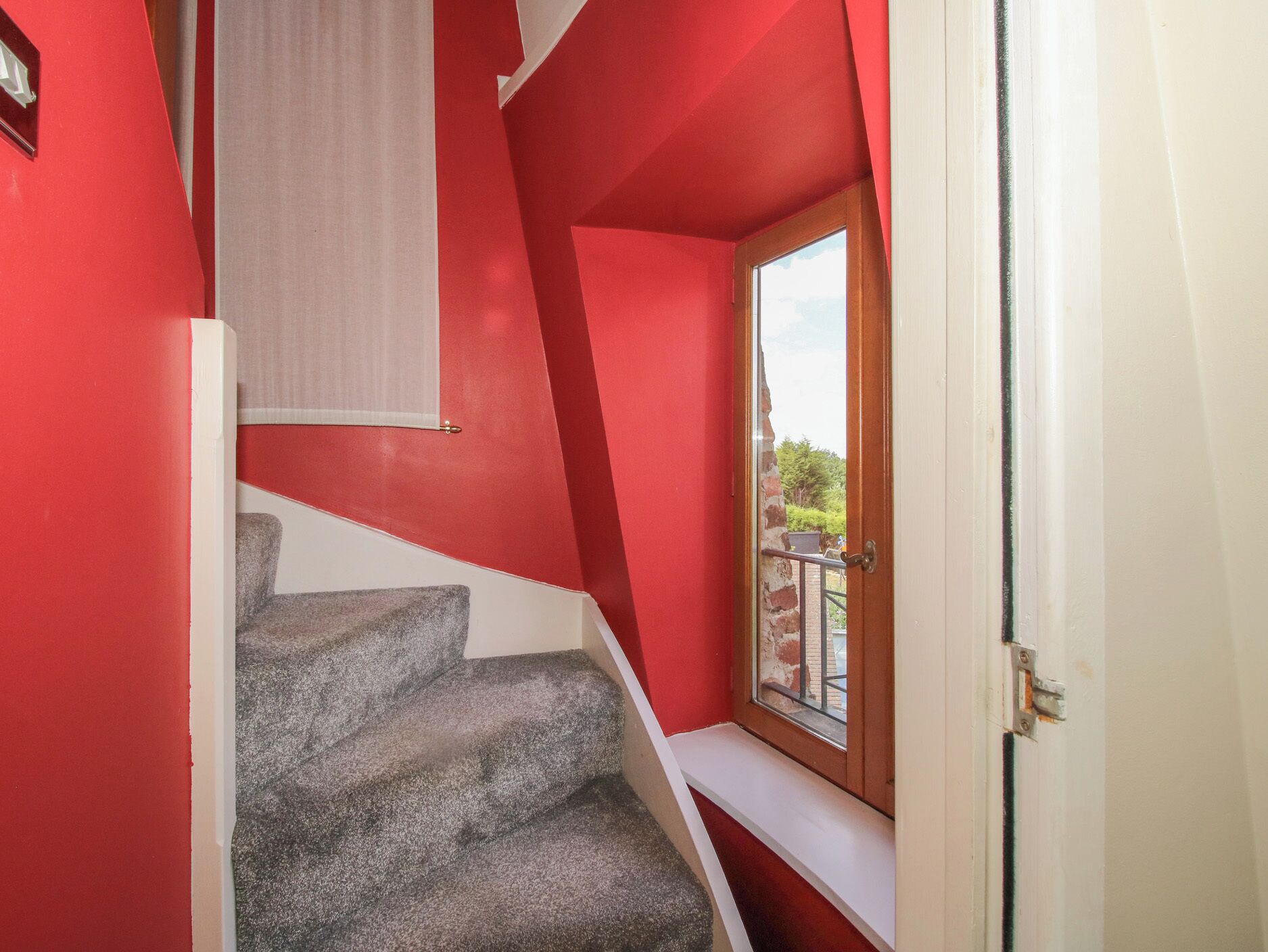Una escalera con un muro rojo y una ventana que da a un espacio al aire libre.