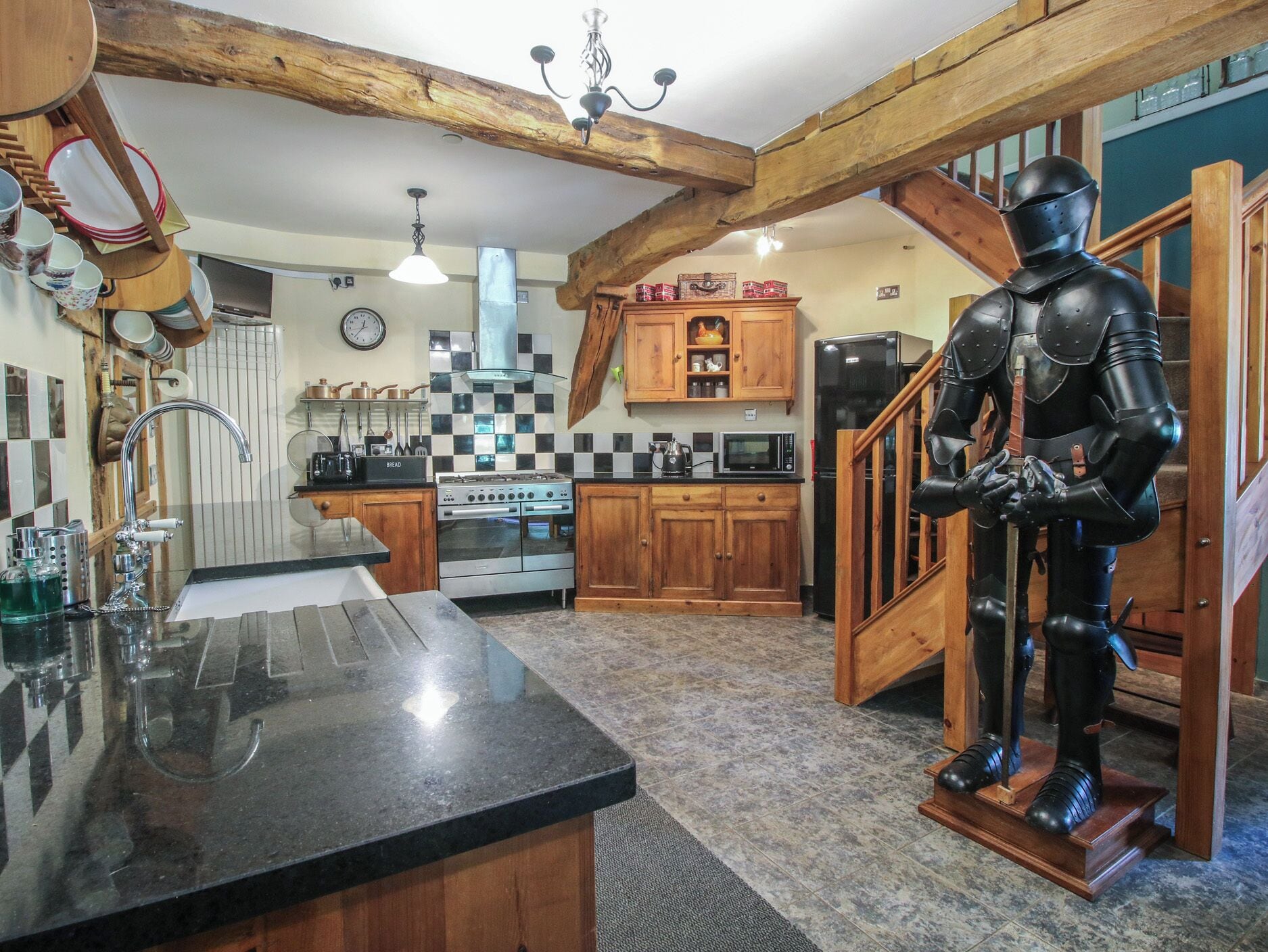 A kitchen with wooden beams, a black countertop, a stove, and a knight statue.