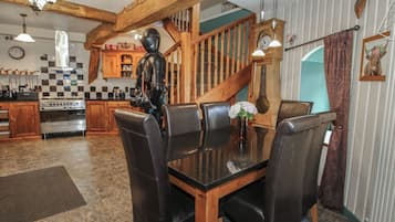 A dining area with a wooden table and leather chairs, a kitchen with checkered tiles, and a staircase with wooden railings.