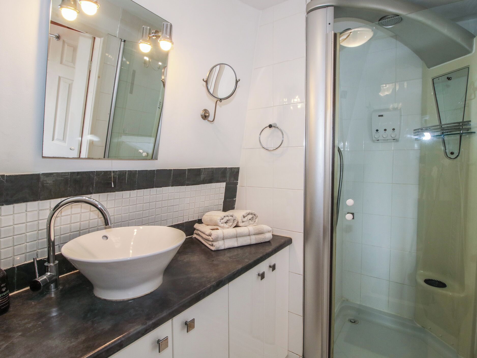 Une salle de bain avec un lavabo blanc, un miroir, une douche en verre et un porte-serviettes.